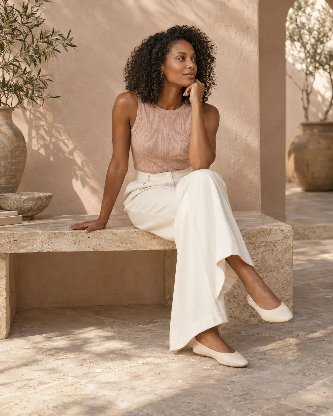 Woman wearing a blush knit top and ivory trousers in a warm minimalist setting